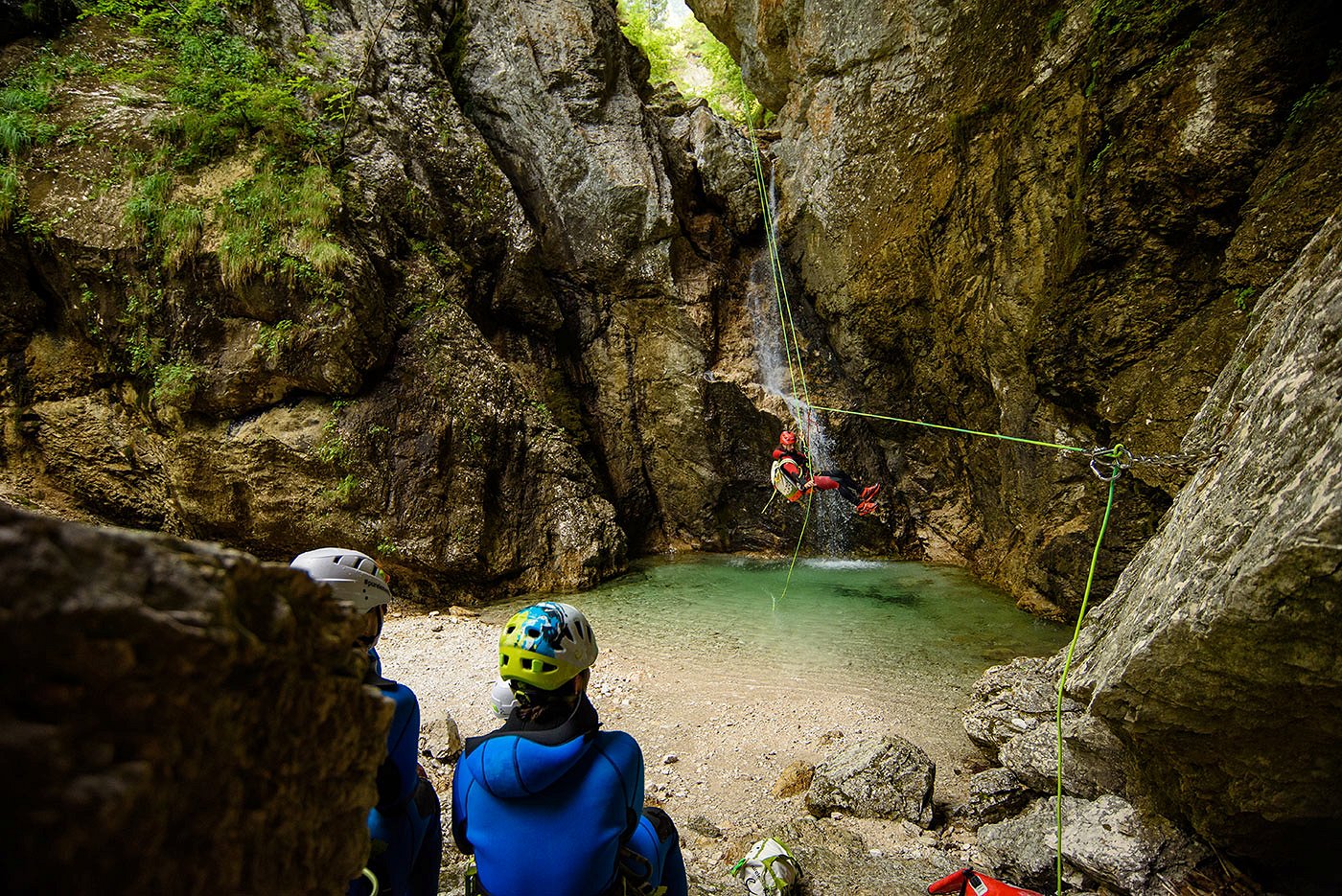 Canyoneer steigt mit einem Seil den Wasserfall hinunter, wo eine Gruppe auf ihn wartet