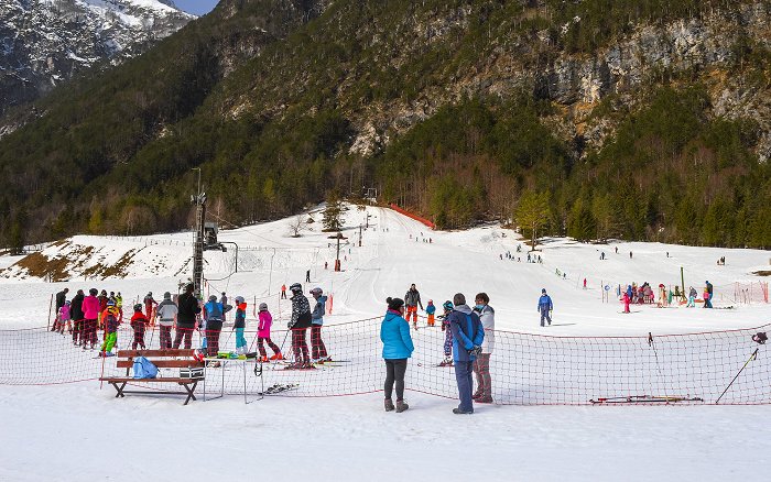 Zasneženo smučišče z dvema vlečnicama, na katerem uživajo otroci vseh starosti.