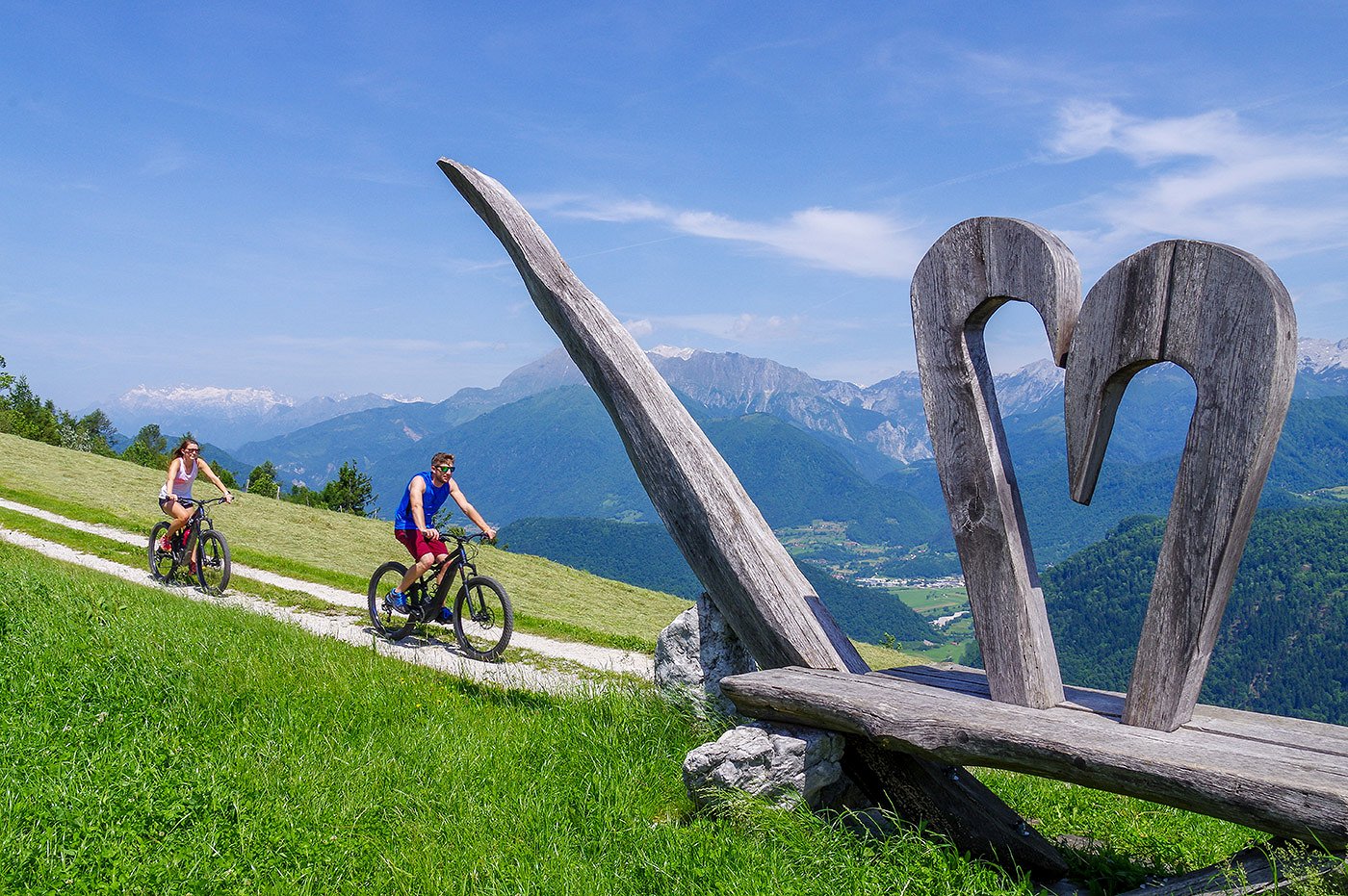 Radfahrer radeln an der Skulptur auf Široko vorbei mit Blick ins Tal