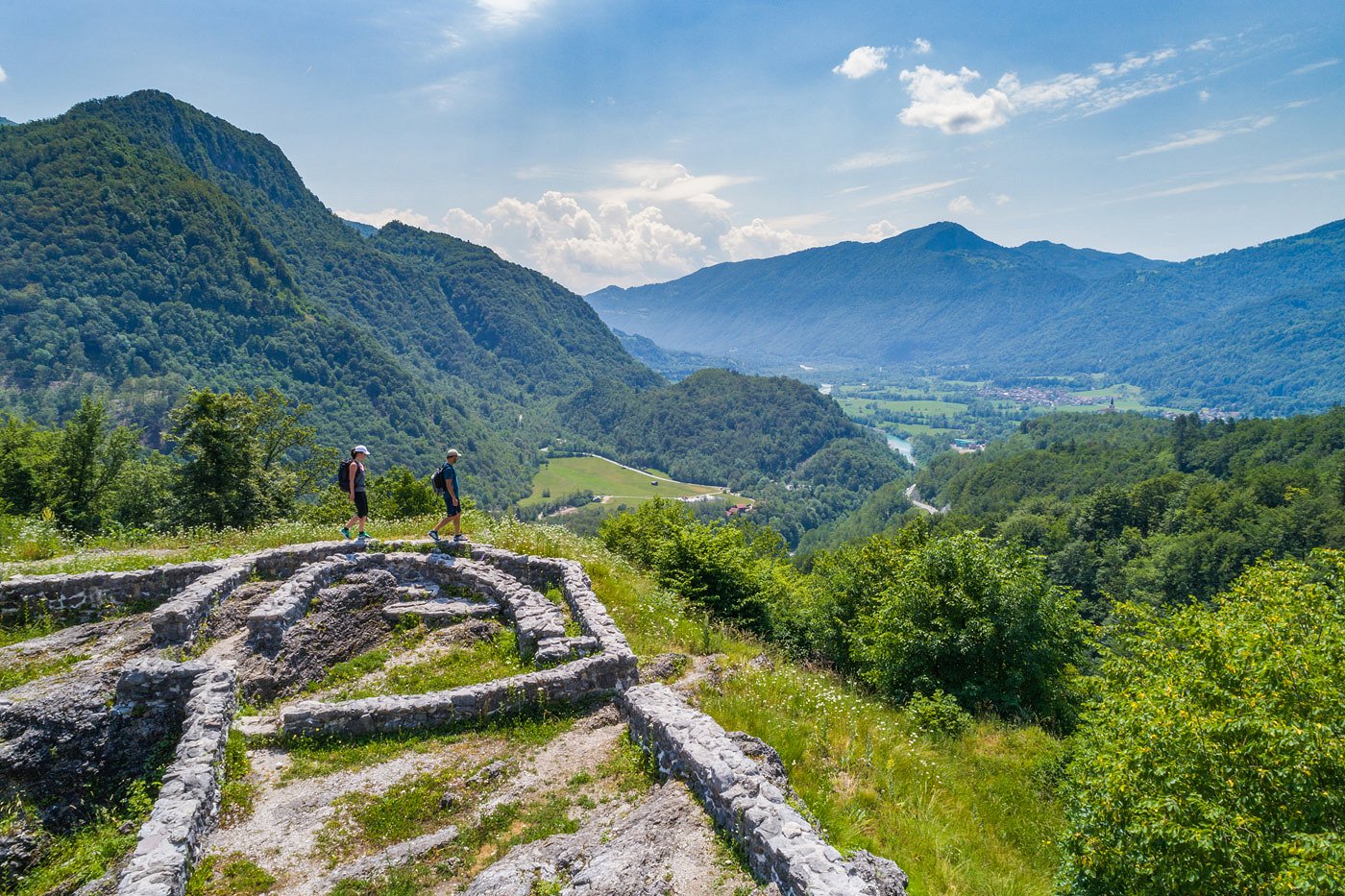 Wanderer wandern entlang der Mauerreste und genießen den Blick auf das Tal, in dem der smaragdgrüne Fluss Soča fließt.