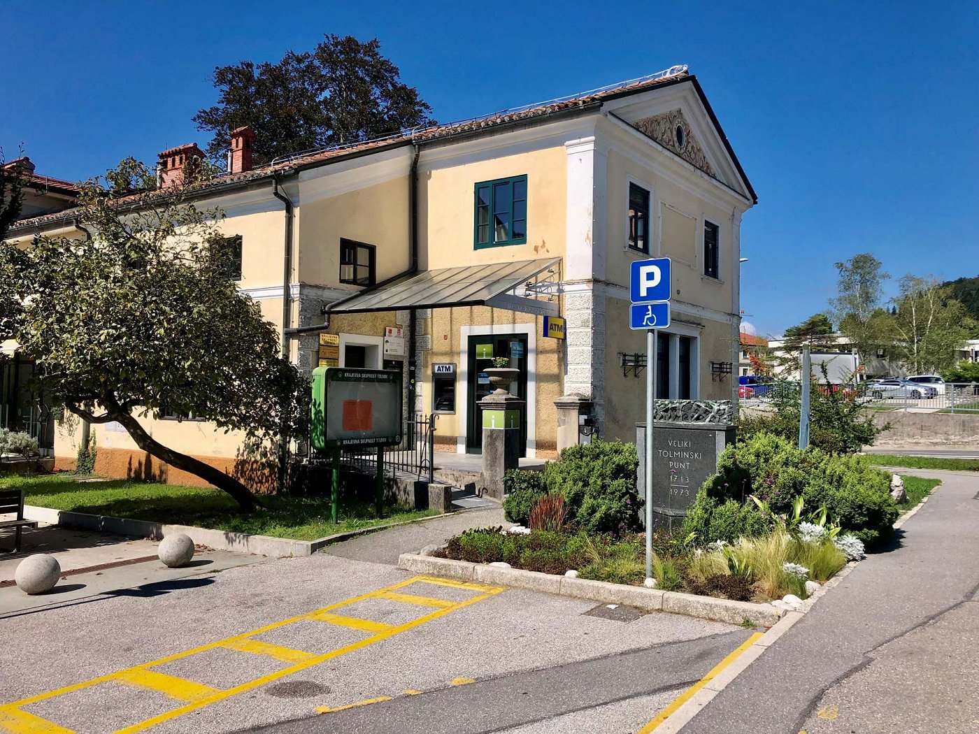 das Gebäude des Touristeninformationszentrums Tolmin im Zentrum von Tolmin, davor ist ein Behindertenparkplatz