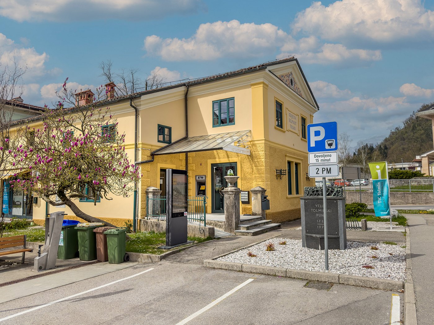 das Gebäude des Touristeninformationszentrums Tolmin im Zentrum von Tolmin, davor ist ein Parkplatz für 15 min