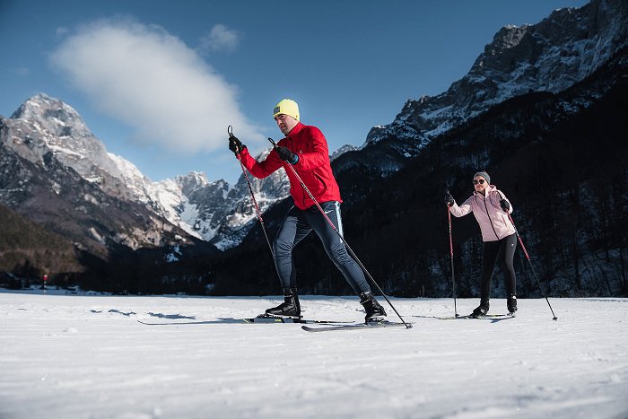 Gli sciatori di fondo si divertono sulla pista preparata con il monte Mangart e la parete della Loška stena sullo sfondo.